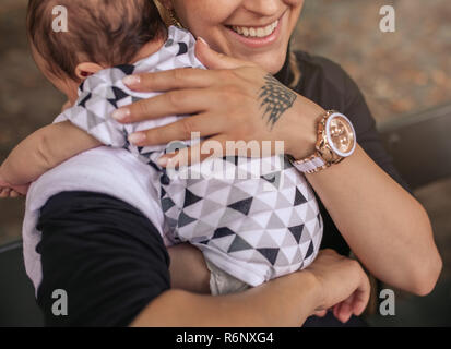 Madre sorridente seduto fuori mentre tiene il suo grazioso baby boy Foto Stock