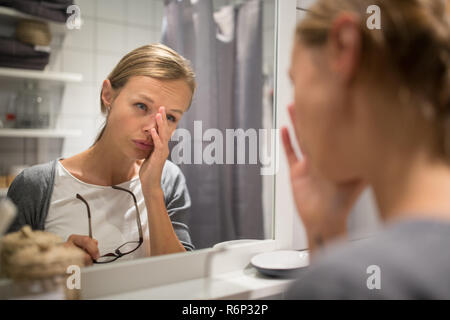 Groggy, giovane donna sbadigliare di fronte a lei lo specchio del bagno al mattino - cercando di svegliarsi e prepararsi per il lavoro (colore immagine dai toni shallow DOF) Foto Stock