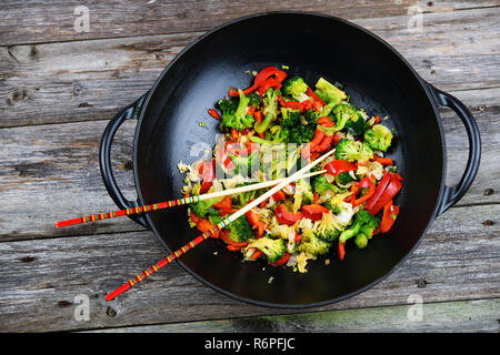 Wok con verdure e bacchette sul terreno in legno Foto Stock