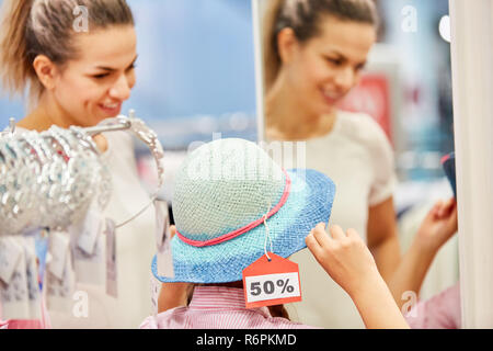 Ragazza al negozio di cappelli durante 50% la vendita con la madre in un boutique hotel Foto Stock