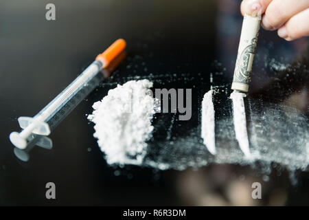La cocaina suddivisa in percorsi su uno sfondo nero. La banconota e la siringa Foto Stock