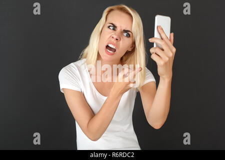 Freestyle. Donna in piedi isolato sul muro nero avente la chiamata video sullo smartphone smorfie arrabbiato per fotocamera close-up Foto Stock
