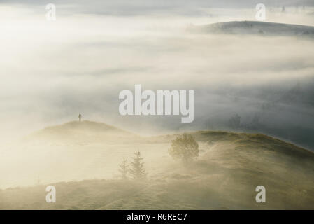 Fotografo di paesaggio con un treppiede in montagna. Mattina nebbia d'autunno. Angolo di Alta Vista dalla collina Foto Stock