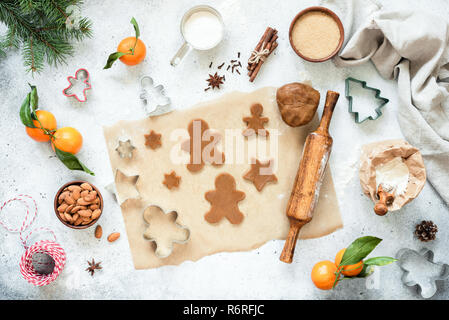 Preparazione di gingerbread cookie. Crudi di panpepato biscotti e pasta biscotto su carta pergamena con decorazioni di Natale intorno a. Vista superiore, piatto Foto Stock