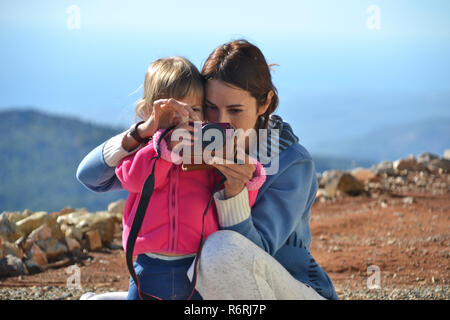 La mamma insegna a sua figlia di scattare le foto. La mamma e il suo bambino tenere la fotocamera insieme e di scattare una foto in montagna. Foto Stock