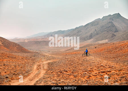 Uomo in mountain bike in maglietta blu nel deserto rosso Foto Stock