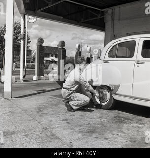 Degli anni Cinquanta, storico i giorni d'oro dell'automobilismo, una stazione di servizio sttendant controlla la pressione su un pneumatico posteriore di un motore Austin auto parcheggiate al Mobilgas 'Ravenscroft' stazione di servizio, Great West Road, London, England, Regno Unito Foto Stock