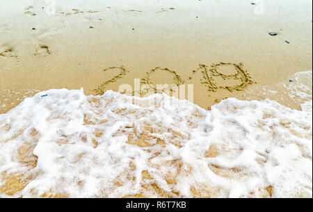 Iscrizione 2019 sulla spiaggia di sabbia con un mare d'onda. Anno Nuovo 2019 è venuta concetto. La fotografia di sfondo. Foto Stock