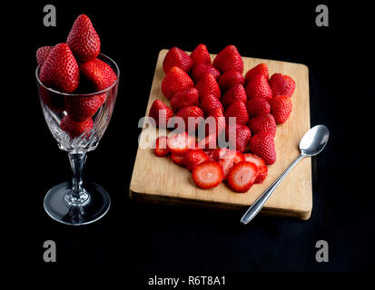 Le fragole in un gass cup besiudes una scheda cuting con più strawberres sulla parte superiore. Foto Stock