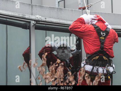 Berlino, Germania. 06 Dic, 2018. Un uomo vestito da Santa Claus si è riflessa in una facciata in vetro e si prepara per la sua missione sul tetto del Charité ospedale per bambini. Dal tetto dell'edificio hanno una cordata giù per i bambini, che hanno aspettato sulle loro stazioni di windows. Successivamente il San Nicola ha visitato le stazioni e presentato presenta. Credito: Paolo Zinken/dpa/Alamy Live News Foto Stock