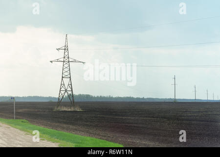 Paesaggio di arato campo scuro terreno con poli elettrici e fili sopra sotto il cielo blu Foto Stock