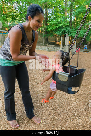 Nailah Wagner spinge la sua figlia, 10-mese-vecchio Emery Wagner, in una oscillazione a Candler Park, Giugno 4, 2014, ad Atlanta, Georgia. Foto Stock