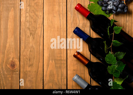 Più bottiglie di vino e le foglie di vite su sfondo di legno. Vista da sopra con copia spazio. Foto Stock