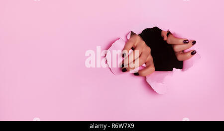 Mani femminili foro di strappo in carta rosa Foto Stock