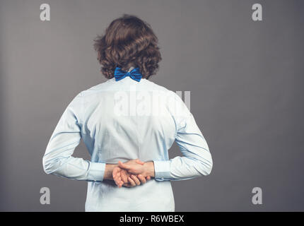 Vista posteriore dell'uomo in maglietta blu e il filtro bow tie. In piedi giovane ragazzo. Vista posteriore di raccolta di persone. Vista posteriore di persona. Isolate su uno sfondo grigio. Un maschio di stand con le sue mani ripiegata in blocco. Foto Stock