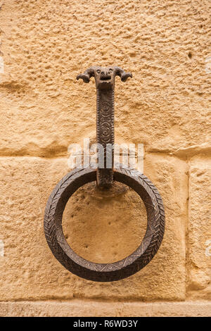 Vecchio ferro battuto anello per cavalli di tethering con testa di ariete, sul blocco di un muro di pietra Foto Stock