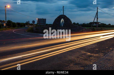 Auto di striature di luce velocizzando il passato un crocevia santa statua in Irlanda rurale Foto Stock