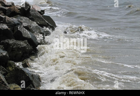 Le onde rompono contro pietre scure Foto Stock