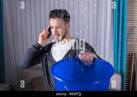 L'uomo la raccolta di acqua nella tazza mentre chiamando l'idraulico Foto Stock