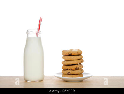 Piccola bottiglia di vetro di latte fresco con candy cane pattern paglia striato sul tavolo accanto alla pila di fatti in casa i biscotti al cioccolato su una piastra. Foto Stock