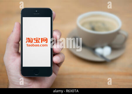 Un uomo guarda al suo iPhone che visualizza il logo di Taobao (solo uso editoriale). Foto Stock