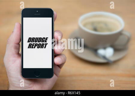 Un uomo guarda al suo iPhone che visualizza il Drudge Report logo (solo uso editoriale). Foto Stock