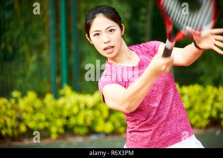 Giovane donna asiatica femmina giocatore di tennis di colpire la palla con diretti Foto Stock