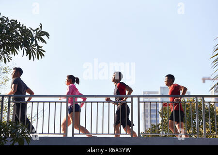 Quattro giovani asiatici runner acceso al mattino passando attraverso un ponte pedonale. Foto Stock