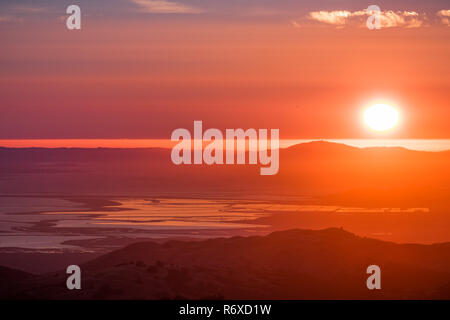 Red Sunset over South San Francisco Bay Area; il sole si riflette nel sale stagni della baia e l'Oceano Pacifico, della superficie visibile in backgrou Foto Stock