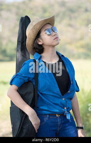 Donna usura hat camminare e portare la sua borsa per chitarra Foto Stock