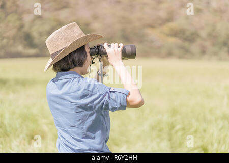 Donna usura hat e tenere premuto binocolo nel campo di erba Foto Stock