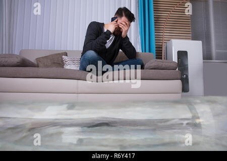 Uomo seduto sul divano chiamando per idraulico Foto Stock