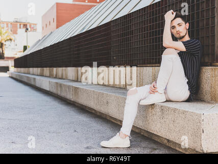 Abito moderno. Moda uomo sedersi sulla panchina e guardare fotocamera. La primavera e l'estate stile di abbigliamento. Foto Stock