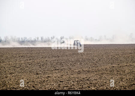 Il trattore erpici il suolo sul campo e crea una nuvola di polvere dietro di essa Foto Stock