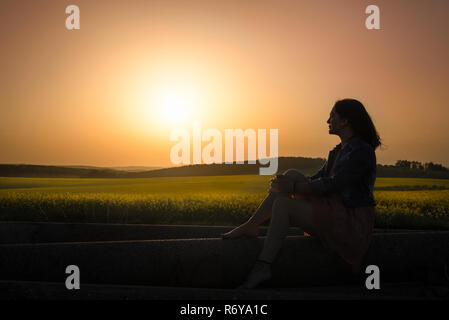 Silhouette di una ragazza e del tramonto su campi di canola Foto Stock