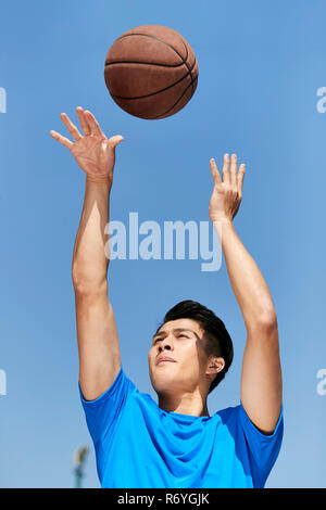 Giovani asiatici giocatore di basket facendo un tiro libero con cielo blu sullo sfondo. Foto Stock