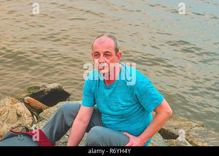 Midle invecchiato uomo seduto sulla riva del lago. Solitudine uomo maturo seduto sulla banca. Concetto di solitudine Foto Stock