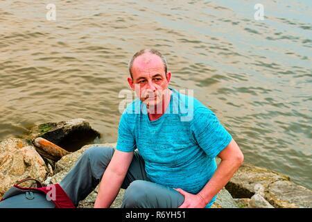 Midle invecchiato uomo seduto sulla riva del lago. Solitudine uomo maturo seduto sulla banca. Concetto di solitudine Foto Stock