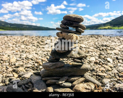 Close-up di pietra cairn su una spiaggia di ciottoli con le montagne e il lago in background Foto Stock