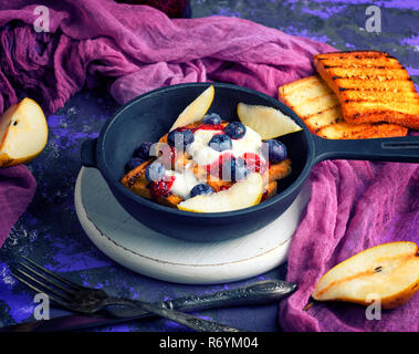 Toast alla francese con frutti di bosco, sciroppo e panna acida in un nero ghisa padella Foto Stock