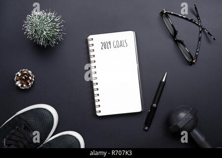 2019 nuovi anni di risoluzioni sport piatto composizione laici. Scarpe nero, nero manubri, bicchieri, vuoto portatile e la decorazione di Natale su nero backgro Foto Stock