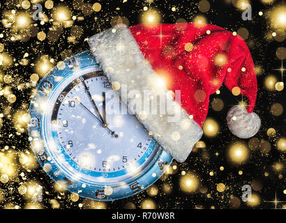 Concetto: Natale e il nuovo anno. Santa è il cappello indossato su un orologio da parete e le frecce indicano l avvicinarsi del nuovo anno di mezzanotte su sfondo nero, oro Foto Stock