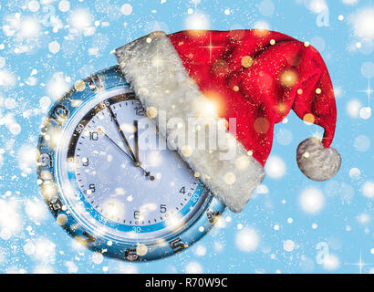 Concetto: Natale e il nuovo anno. Santa è il cappello indossato sull'orologio a muro e le frecce mostrano ormai imminente nuovo anno di mezzanotte su sfondo blu, golden caduta Foto Stock