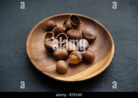 Le castagne sul piatto di legno su sfondo scuro. Foto Stock