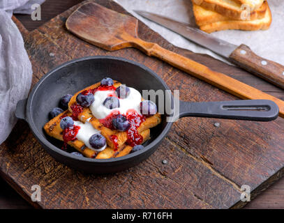 Toast alla francese con frutti di bosco, sciroppo e panna acida in un nero ghisa padella Foto Stock