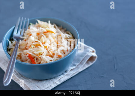 Vaso in ceramica di gustoso cavolo fermentato con forcella in piedi sul tovagliolo sul tavolo in legno Foto Stock