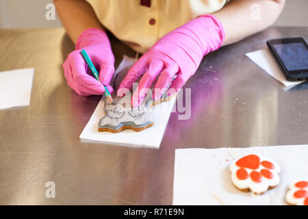 Donna con le mani in mano nel processo di disegno sul nuovo anno gingerbread cookie su un tavolo in metallo. Foto Stock