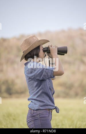 Donna usura hat e tenere premuto binocolo nel campo di erba Foto Stock