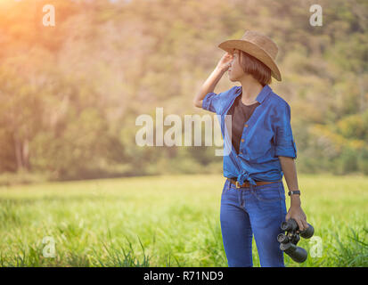 Donna usura hat e tenere premuto binocolo nel campo di erba Foto Stock