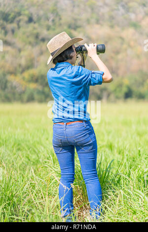 Donna usura hat e tenere premuto binocolo nel campo di erba Foto Stock